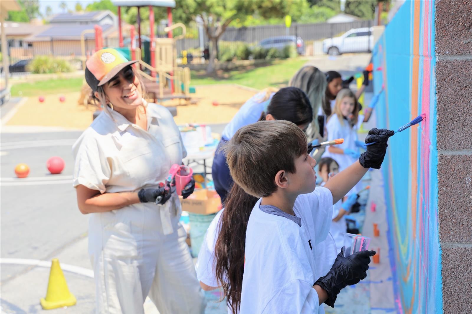 Student with mural artist carla roque painting a mural at hermosa drive